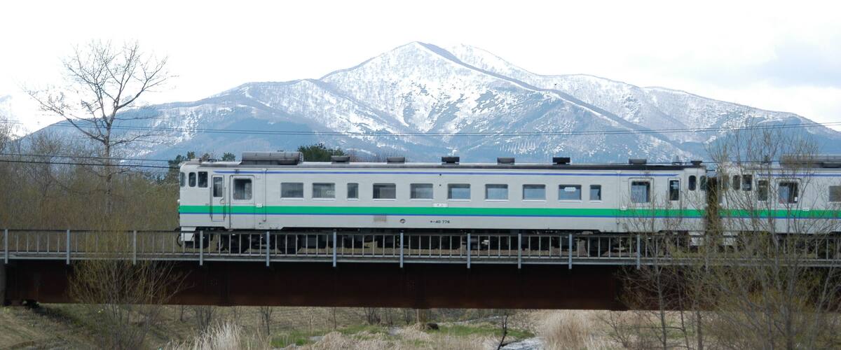 A train crossing a bridge over a river with a mountainous backdrop.