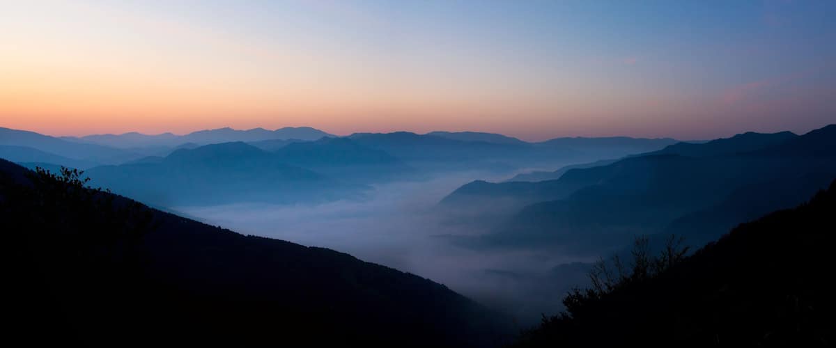 A mountain range at sunrise with mist-covered valleys.