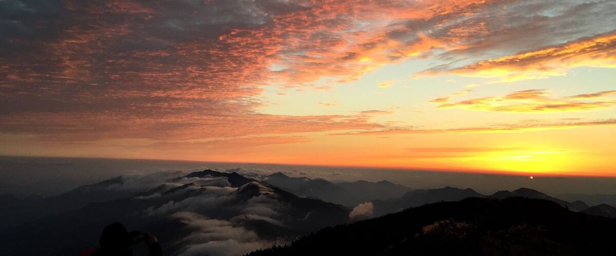A mountain range with a sunset and clouds.