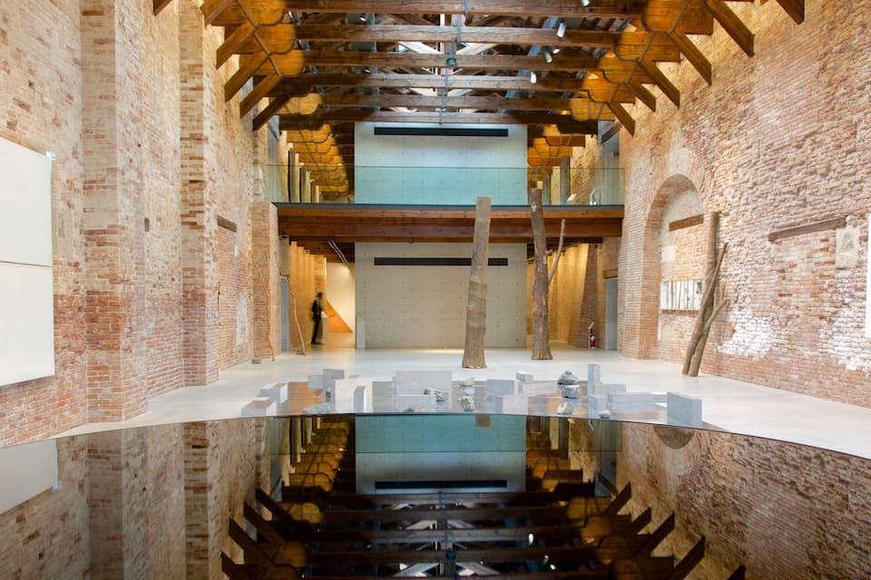 An indoor art gallery with brick walls, wooden beams, and a reflective floor.