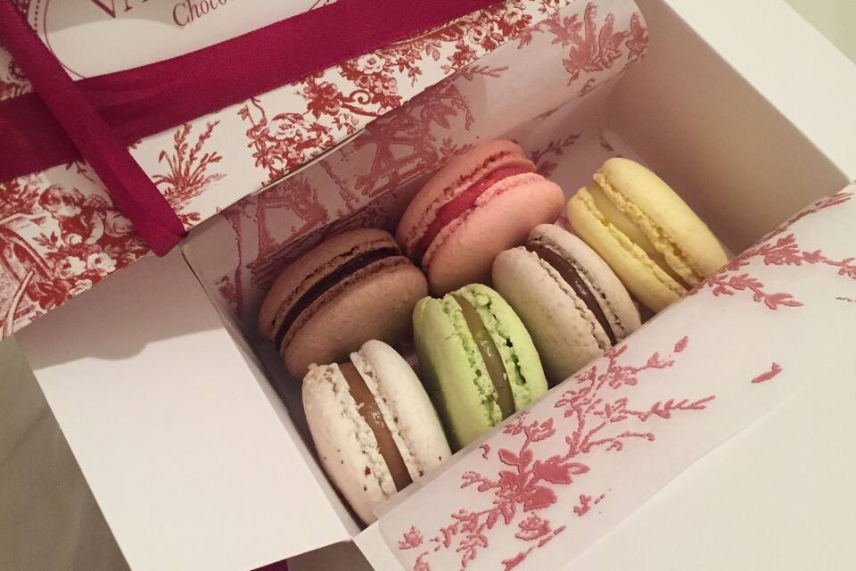 Uma caixa com macarons variados, design floral e um laço vermelho.