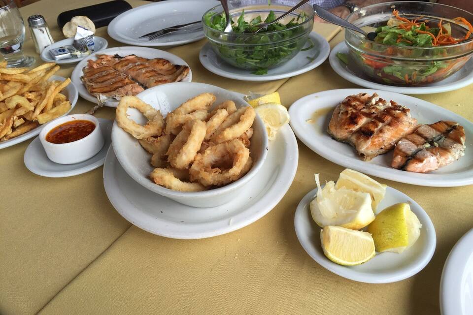 Uma mesa com vários pratos, incluindo lula frita, salmão grelhado e uma salada.