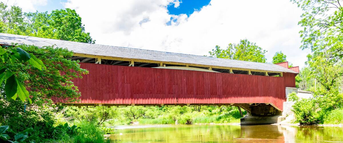 A red covered bridge over a calm river with lush greenery around.