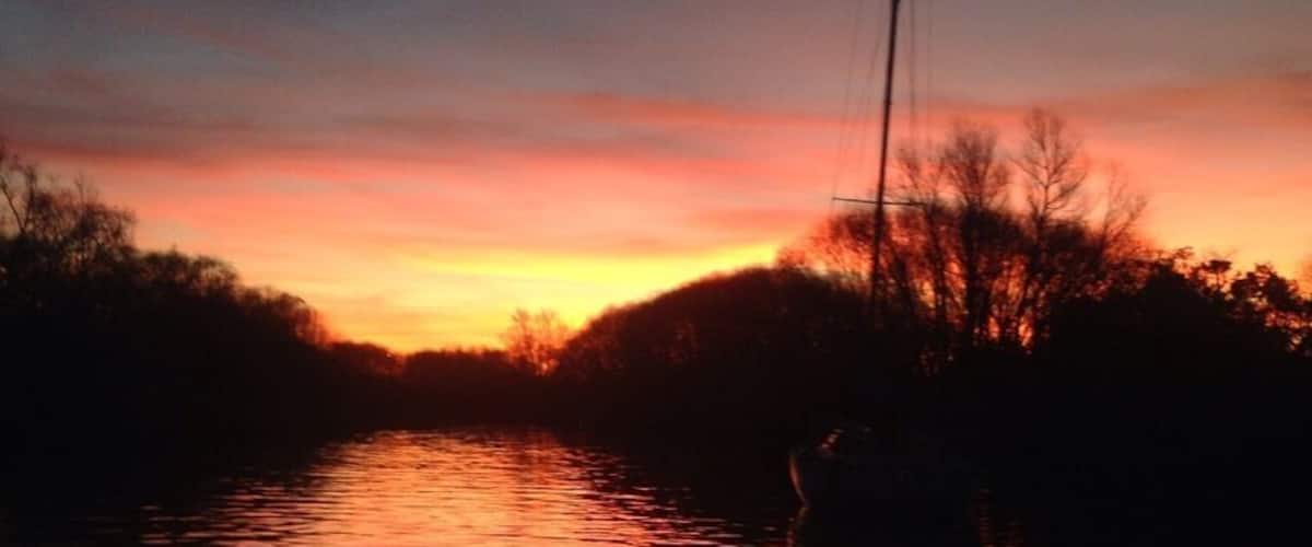 A sunset over a calm river with a boat in the foreground.