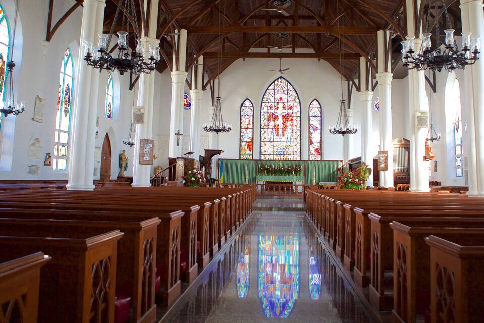 Interior de iglesia con bancos de madera, vidrieras de colores y un altar central.