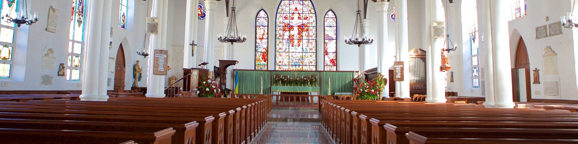 Interior de igreja com bancos de madeira, vitrais e altar central.