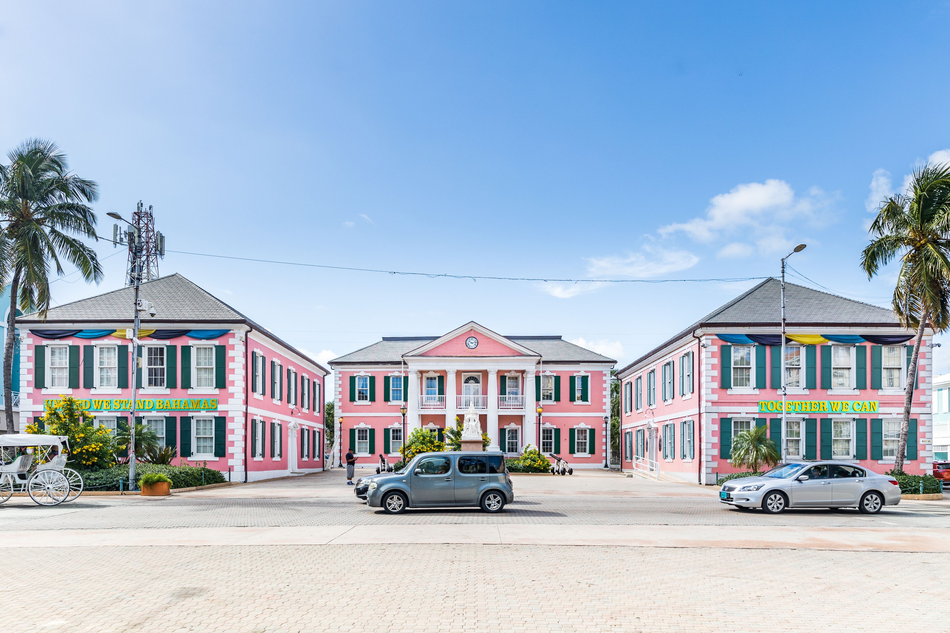 A pink building with 'The West End and Bahamas' sign, a small car, and palm trees.