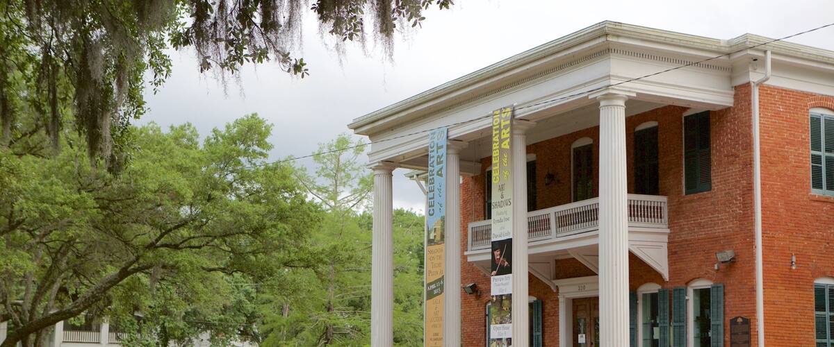A historic building with columns and banners, surrounded by trees and a brick fence.
