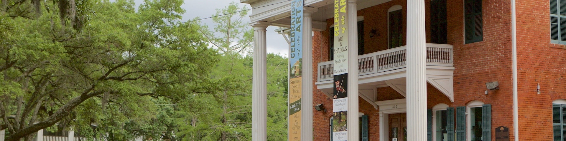 A historic building with columns and banners, surrounded by trees and a brick fence.