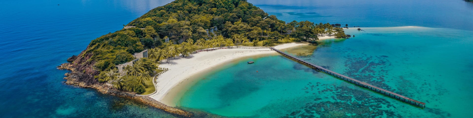 A tropical island with a white sandy beach, clear turquoise waters, and a wooden pier.