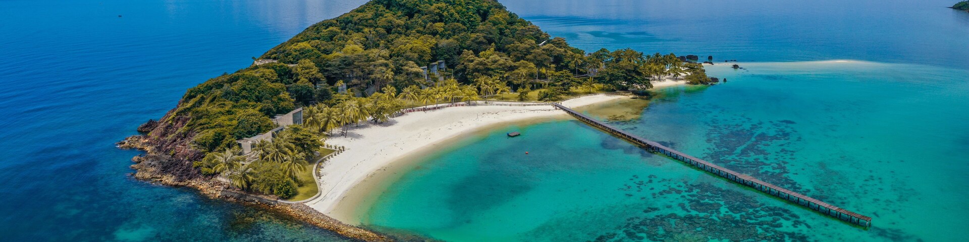 A tropical island with a white sandy beach, clear turquoise waters, and a wooden pier.