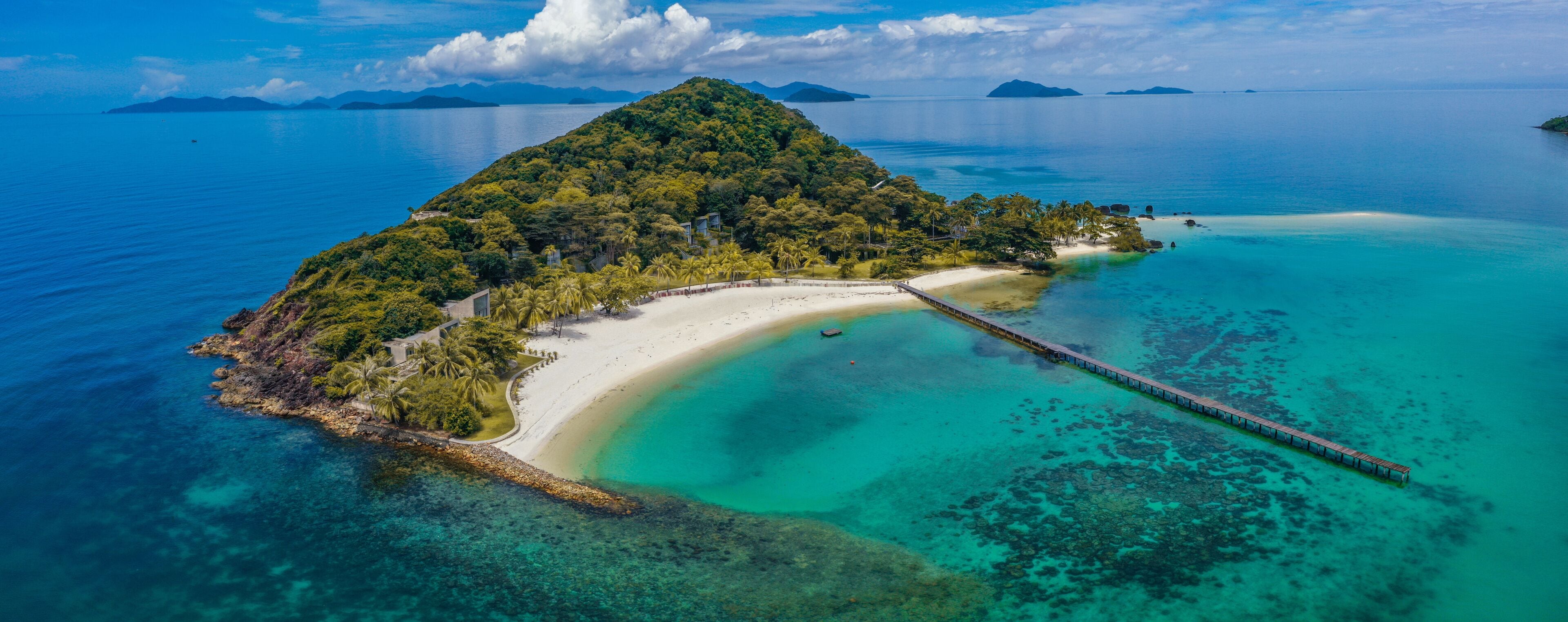 A tropical island with a white sandy beach, clear turquoise waters, and a wooden pier.