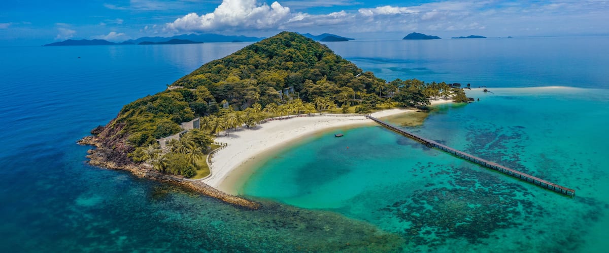 A tropical island with a white sandy beach, clear turquoise waters, and a wooden pier.