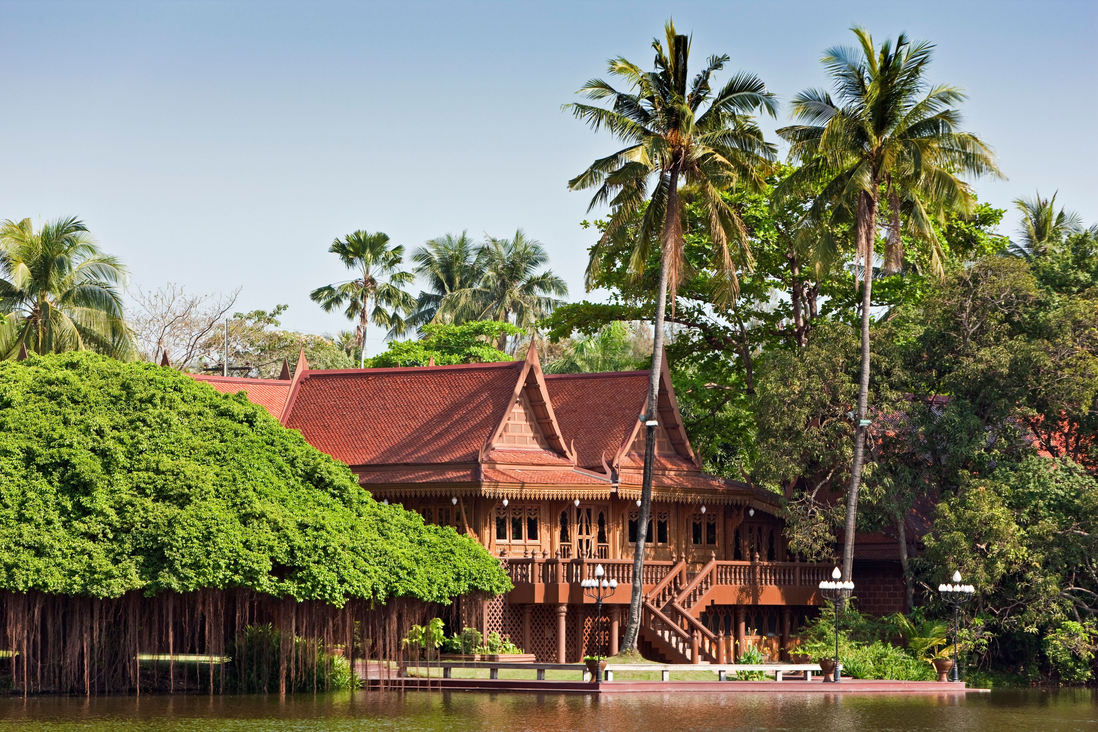 A traditional wooden building with a red roof, surrounded by lush greenery and palm trees.