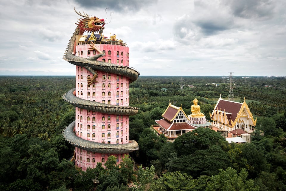 A pink multi-tiered pagoda with a dragon on top, surrounded by lush greenery and traditional architecture.