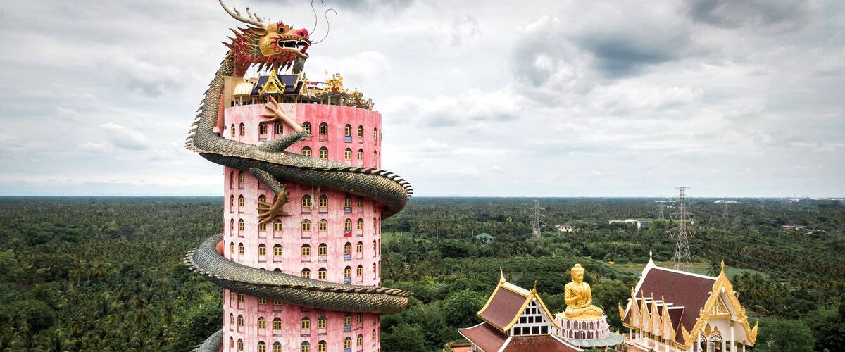 A pink multi-tiered pagoda with a dragon on top, surrounded by lush greenery and traditional architecture.