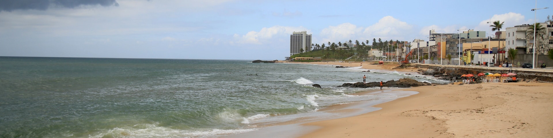 Ein Strand mit Wellen, blauem Himmel und Gebäuden entlang der Küste.