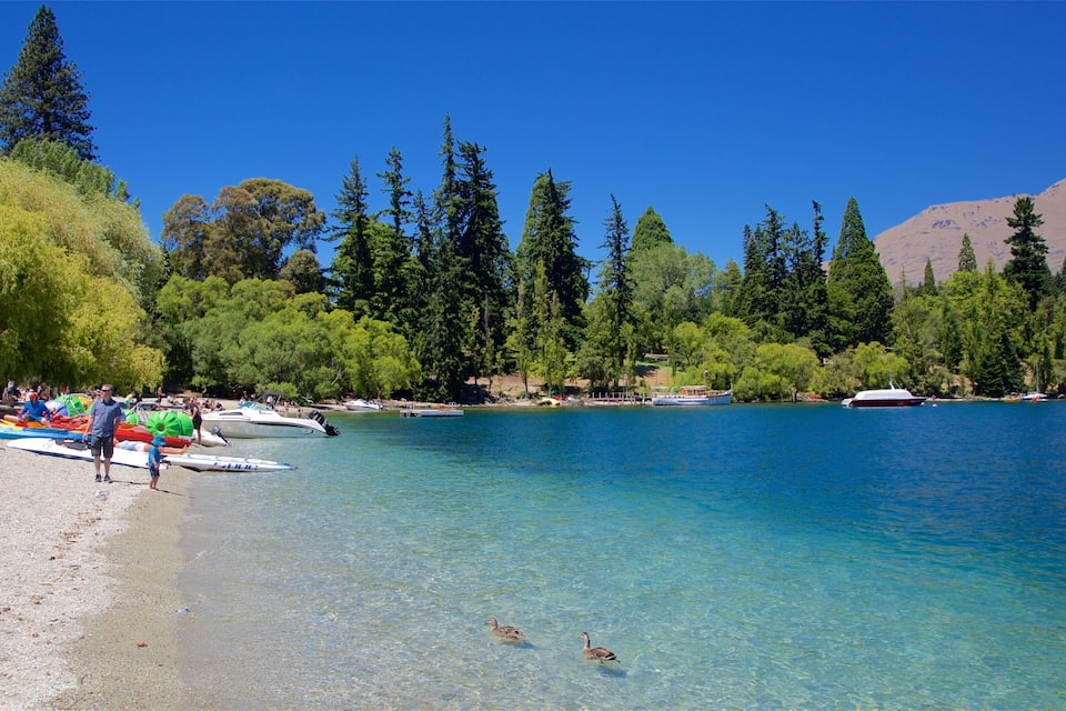 Un llac tranquil amb barques, una platja sorrenca i arbres densos.