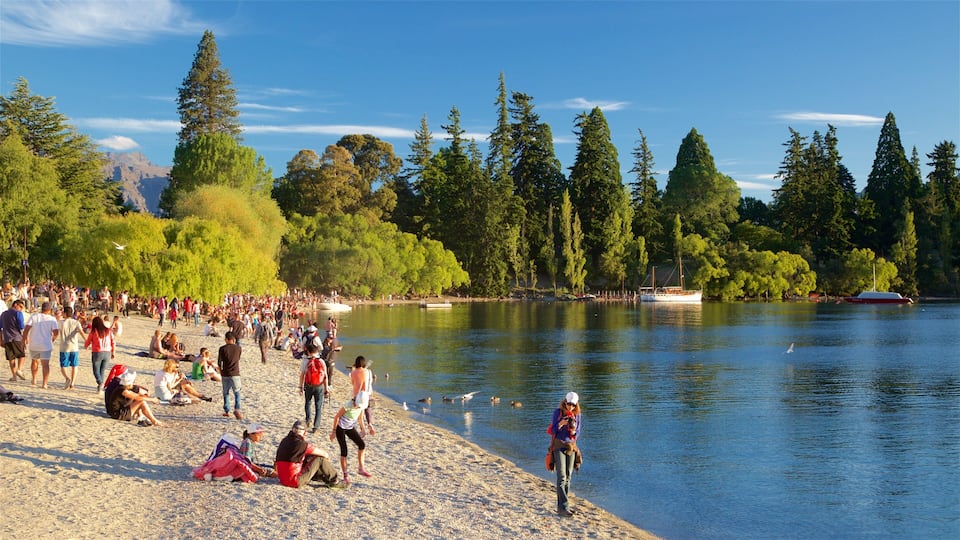 A crowded lakeside beach with people relaxing and a boat docked near the shore.