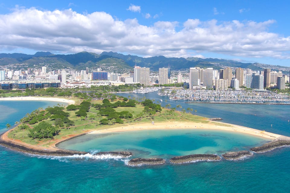 A coastal cityscape with a marina, a beach, and mountains in the background.
