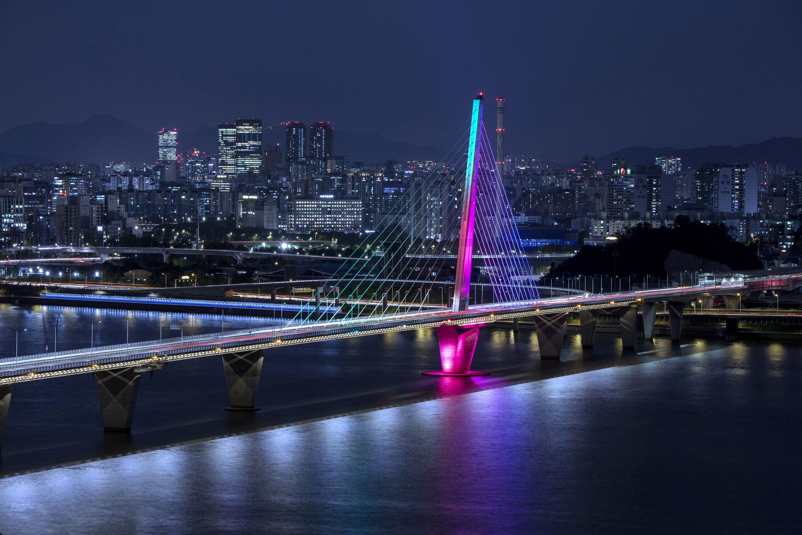 Gangseo-gu, Seoul, South Korea - October 26, 2022: High angle and night view of World Cup Bridge with colorful illumination on Han River against Olympic Boulevard and apartments
