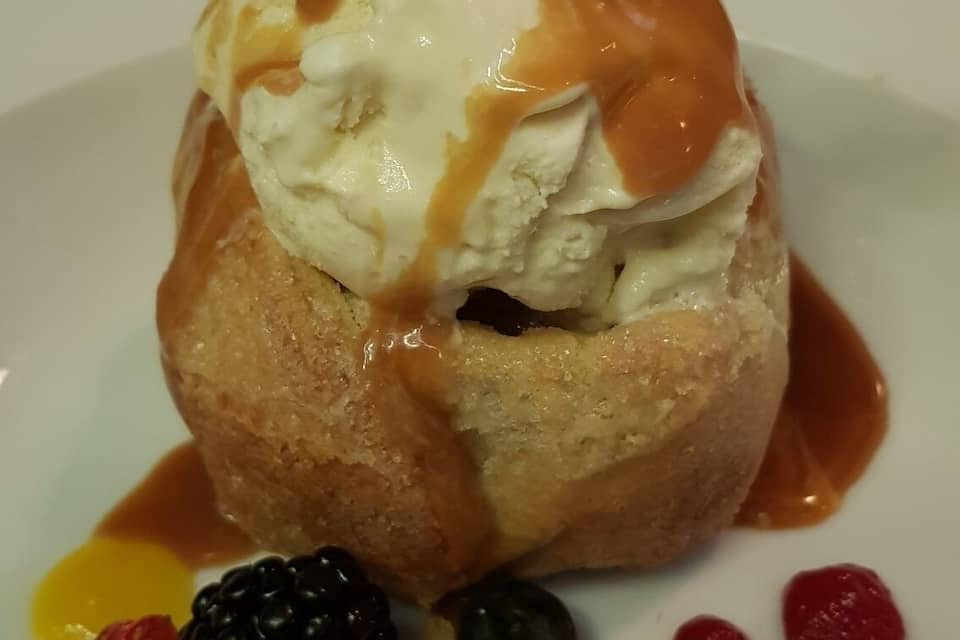 A dessert with ice cream, caramel sauce, and fruit garnishes on a plate.