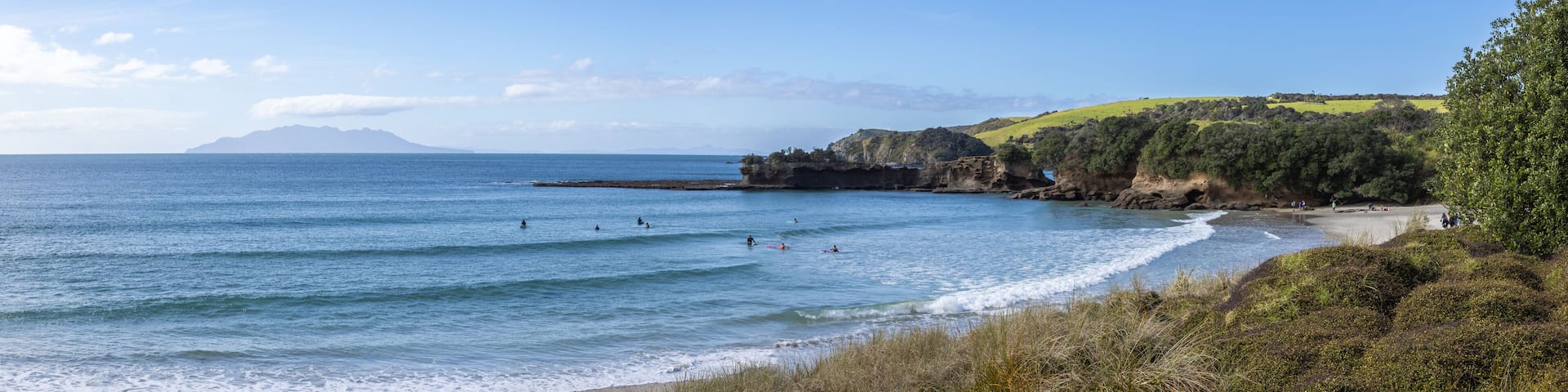 A coastal landscape with a beach, ocean waves, and distant mountains.