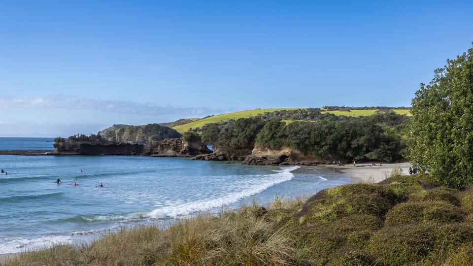 A coastal landscape with a beach, ocean waves, and distant mountains.