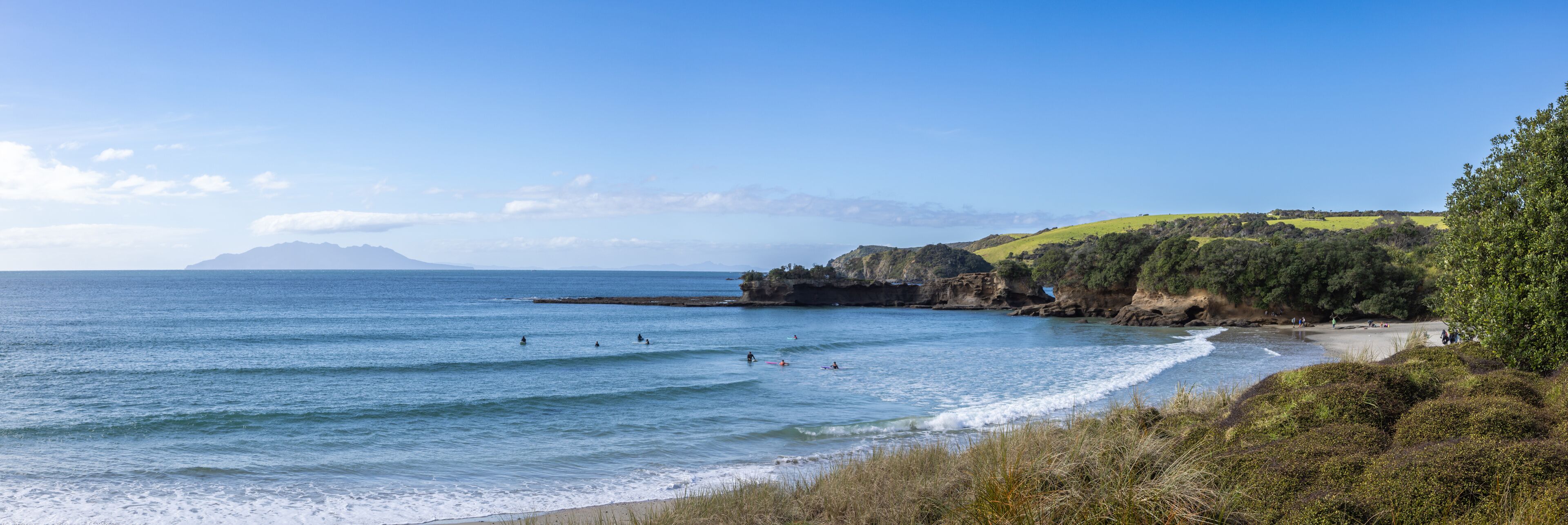 A coastal landscape with a beach, ocean waves, and distant mountains.