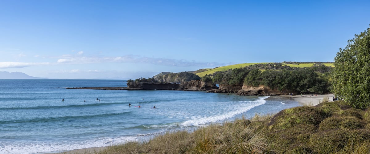 A coastal landscape with a beach, ocean waves, and distant mountains.