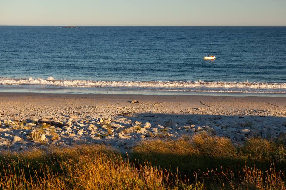Une plage rocheuse avec des vagues, un bateau et une île au loin.