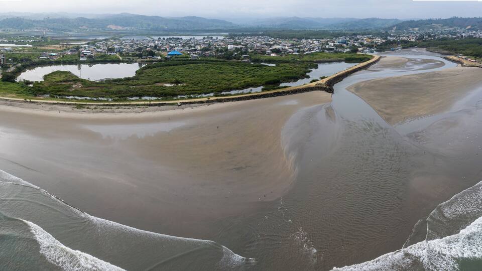 A coastal city with a beach, a river, and a distant mountain range.