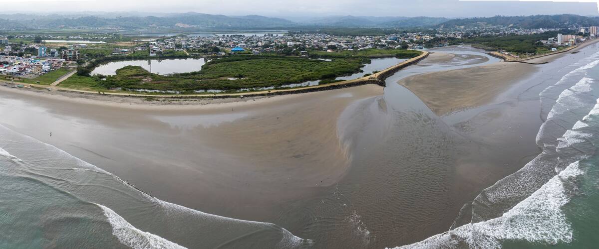 A coastal city with a beach, a river, and a distant mountain range.