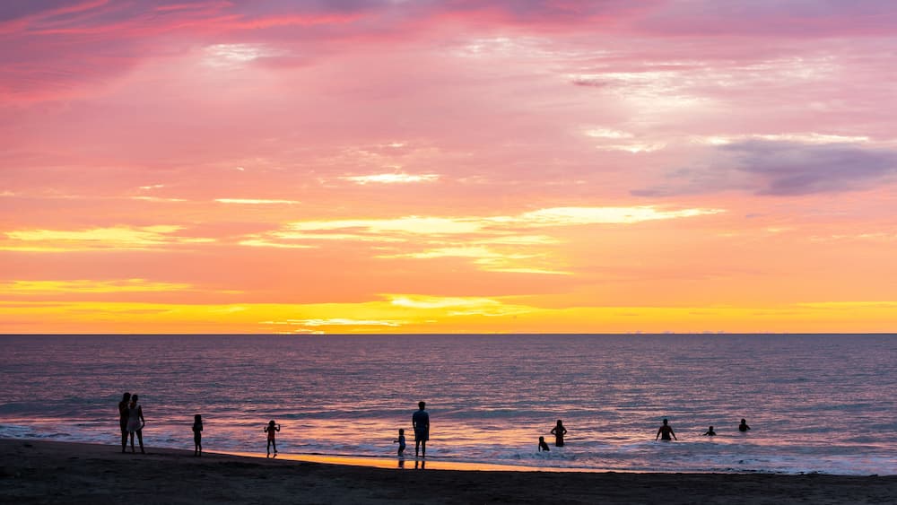 Une plage au coucher du soleil, avec des silhouettes de personnes et un ciel aux couleurs vives.