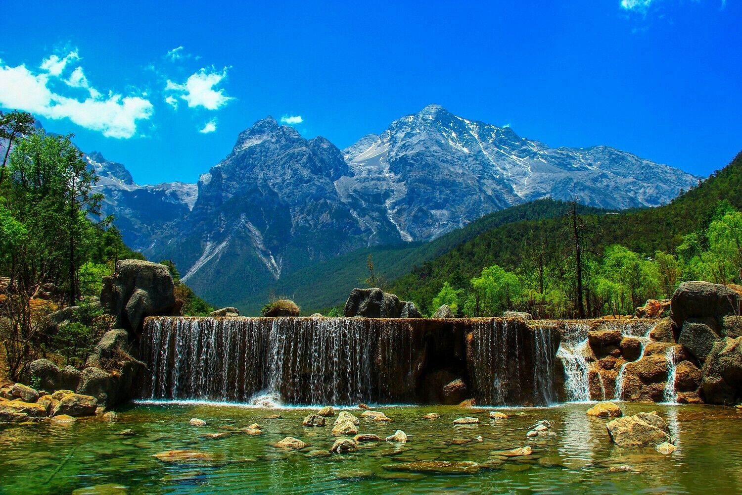 A waterfall in a forest with mountains in the background.