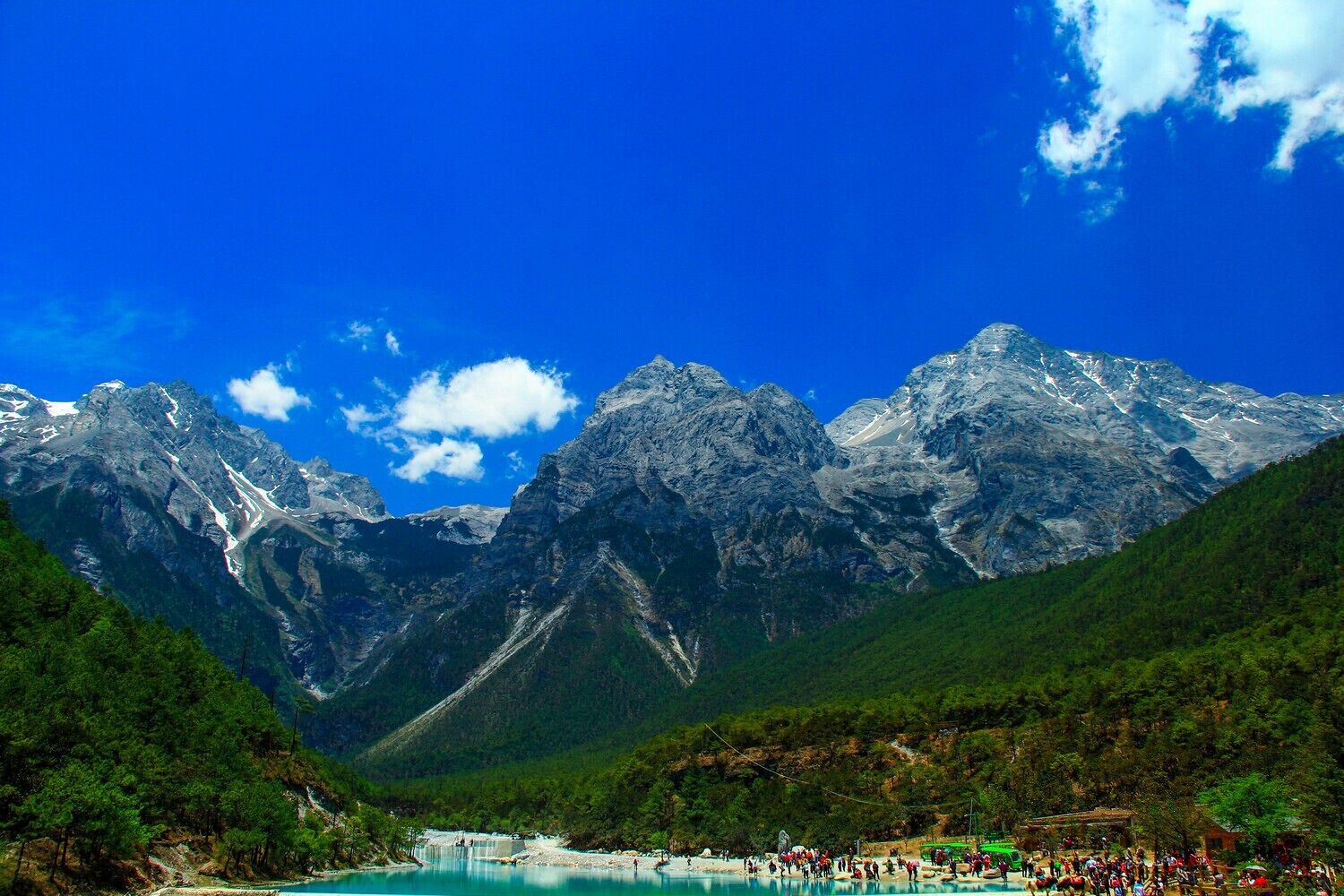 A mountain range with a lake and a crowd of people at the lake's edge.