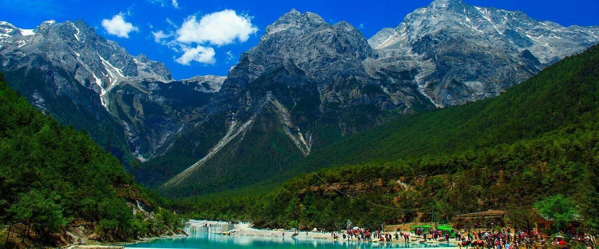 A mountain range with a lake and a crowd of people at the lake's edge.