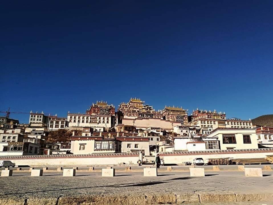 Paisaje montañoso con arquitectura tibetana tradicional, incluyendo edificios de varios niveles y techos dorados.