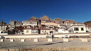 Paisaje montañoso con arquitectura tibetana tradicional, incluyendo edificios de varios niveles y techos dorados.