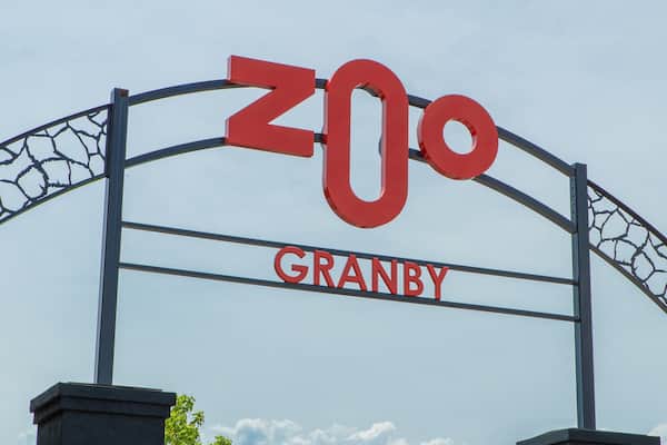 Une grande enseigne rouge avec le mot « ZOO » écrit en haut et le mot « GRANBY » en dessous, fixée sur une structure arquée en métal.