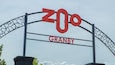 Ein großes, rotes Schild mit der Aufschrift 'ZOO' und darunter 'GRANBY', an einer metallenen Bogenkonstruktion befestigt.