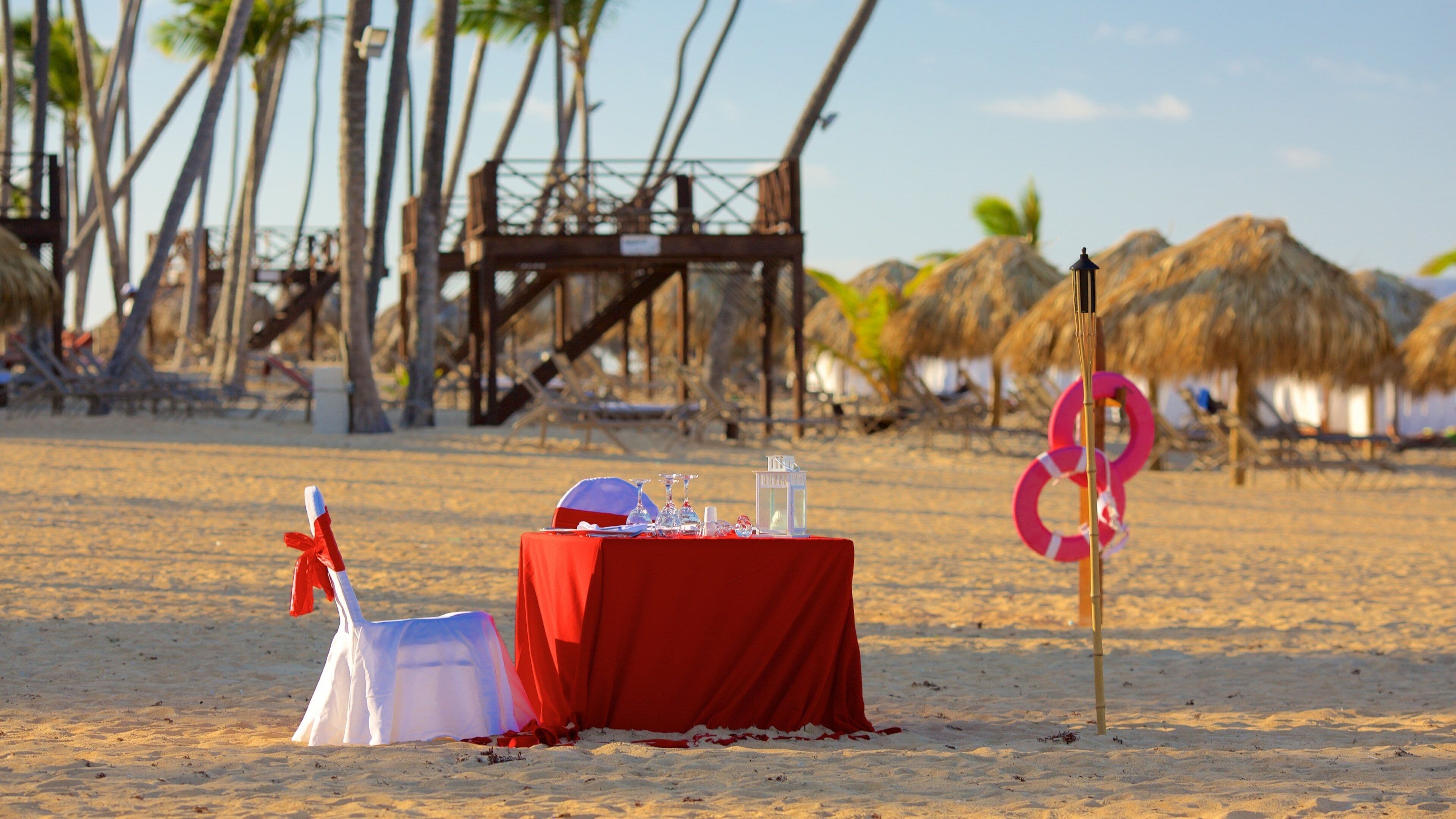 A beach setting with a red table, white chair, and a lifebuoy.