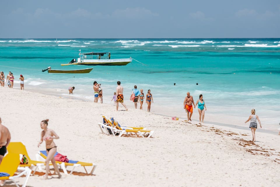 A beach with people sunbathing, walking, and a boat in the water.