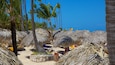 A beach with thatched umbrellas, palm trees, and a clear blue sky.