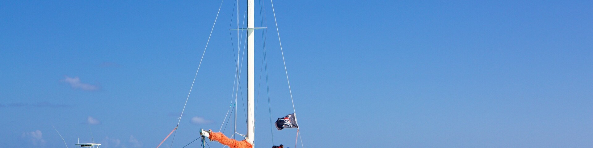 Un velero con bandera de calavera y tibias, rodeado de otras embarcaciones en aguas turquesas.