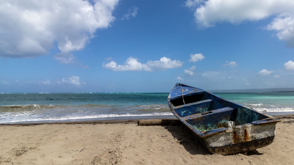A beach with a blue boat on the sand and the ocean in the background.