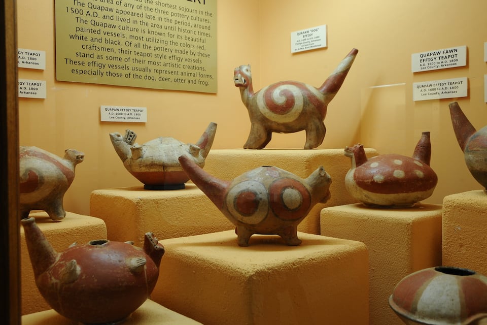A display of ancient pottery with animal figures, including a turtle and a dog, in a museum setting.