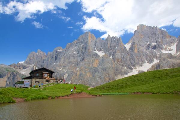 Eine Berghütte vor einem See, umgeben von felsigen Gipfeln und wolkenlosem Himmel.