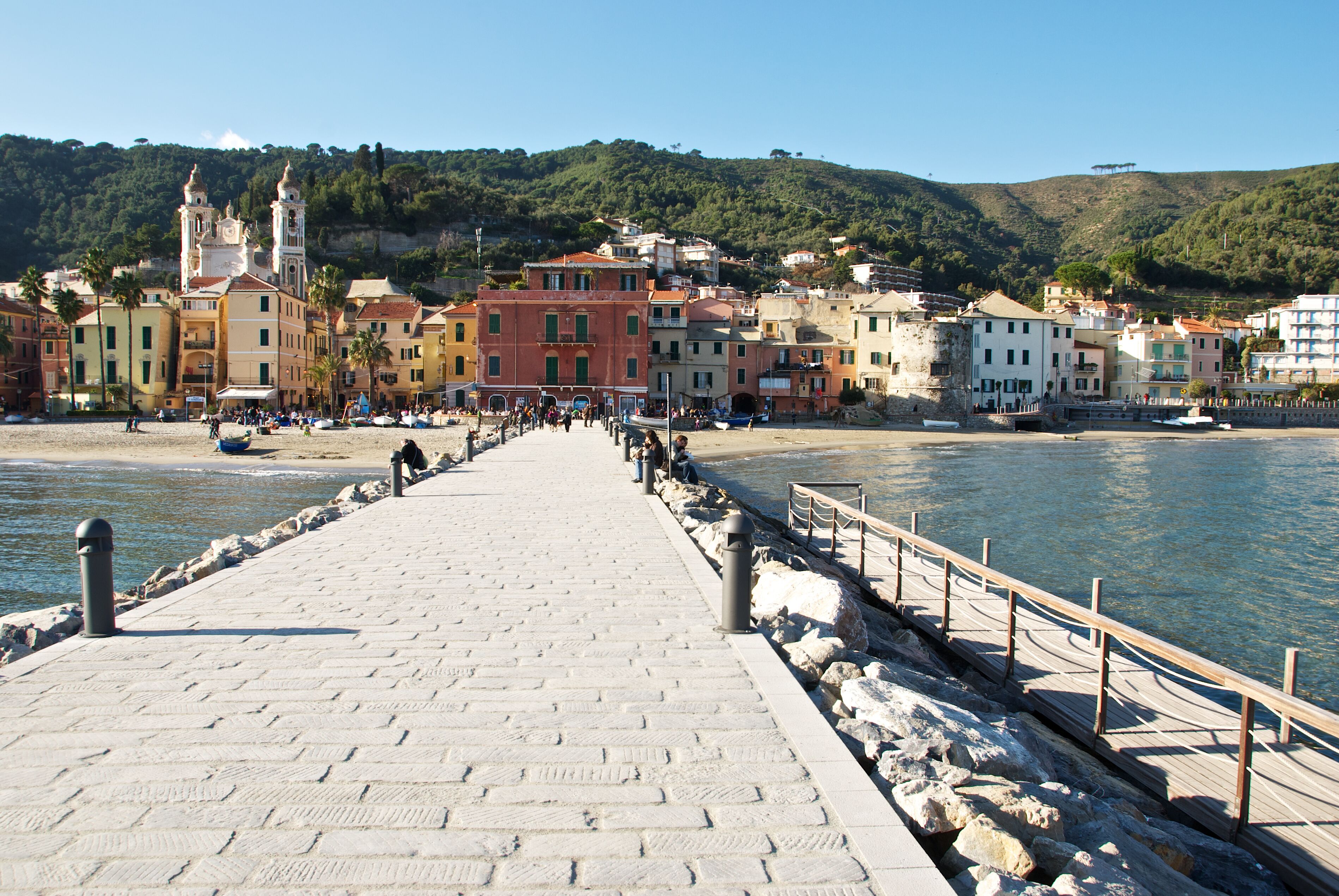 A paved promenade leading to a beach with colorful buildings and a church in the background.