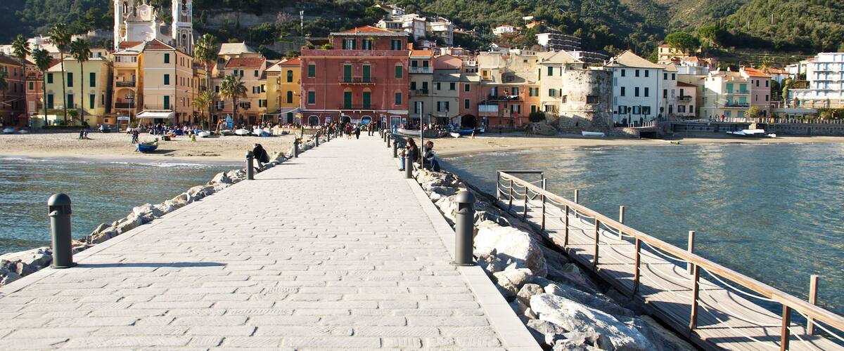A paved promenade leading to a beach with colorful buildings and a church in the background.